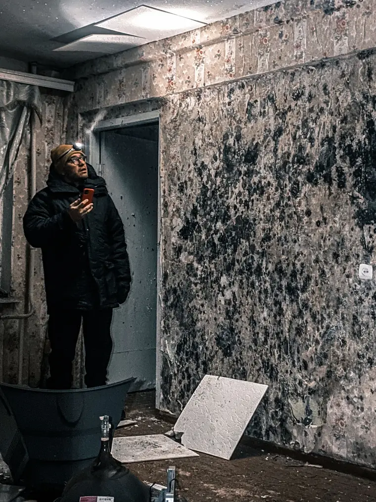 Inspecting heavy mold growth on a wall by headlamp, phone camera in hand